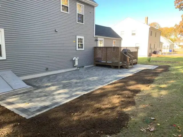 Paver patio installed beside a house with a gray siding